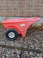 Side view of the red plastic Little Tikes wheelbarrow toy showing two black wheels and the main carrying compartment.