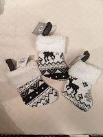 Set of three mini Christmas stockings on a beige patterned surface. Two with black and white reindeer patterns, one plain grey with white fluffy cuff.