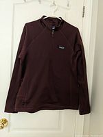 Full view of maroon Patagonia pullover hanging on door, showing front side with quarter zipper collar.