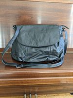 Front view of the large black leather purse showing the full size and fold-over flap with adjustable shoulder strap.