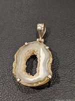 Front view of quartz geode slice pendant showing hollow center with visible quartz crystals inside. The stone has white, beige, and light brown layered edges in silver prong setting.