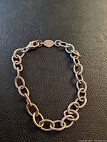 Full view of the sterling silver chain link bracelet laid flat on a black textured surface, showing overall design and lobster clasp.