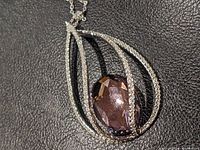 Close-up of the Swarovski pendant showing teardrop shape with clear crystals and central purple faceted crystal.