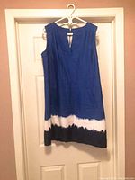 Blue linen shift dress hanging on door, showing front view and hem detail