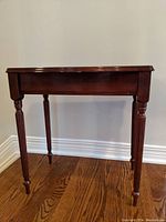 Front view of the small Bombay Company wooden table showing scalloped front edge and four turned legs.