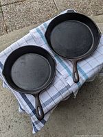 Top view of two cast iron pans on a cloth, showing size and condition of cooking surfaces and handles.