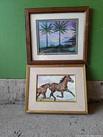 Two medium-size original nature paintings in frames, one with glass showing palm trees and ocean, the other without glass showing running horses.
