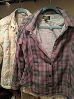 Two jackets hanging side by side on blue hangers, one purple plaid, one cream sherpa-lined