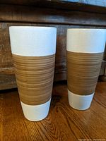 Pair of two-tone tall vases with white crackle finish on top and bottom, brown grooved midsection, standing on wooden floor.