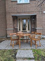 Full view of round dining table with four chairs outdoors in front of a brick house