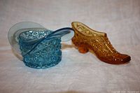 Blue clear glass top hat and amber daisy button shoe together on neutral fabric background