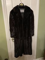 Front view of coat hung on door showing full-length black mink fur and collar