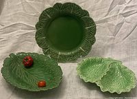 Three green ceramic serving dishes with leafy motifs on fabric background