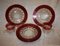 Six sandwich plates stacked, visible deep red and gold design with clear center; creamer and sugar bowl set in front.