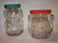Photo of two Kraft Collector teddy bear glass jars on neutral background showing front and lid colors