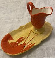 Ceramic butter pitcher on lobster-themed butter tray with orange lobster and yellow leaf-shaped base.
