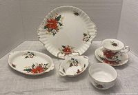 Overview of six pieces in Royal Albert Pointsettia Yuletide collection showing floral poinsettia pattern with gold trim on white bone china.