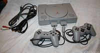 Photo of PlayStation 1 console with two wired controllers and required wiring (power and AV cables).