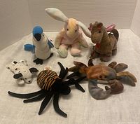 Collection of six TY Beanie Babies including a white rabbit, blue jay, crab, spider, cow, and dragon displayed together.
