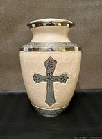 Front view of ivory urn with detailed silver cross and decorative bands.