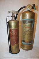 Two vintage brass fire extinguishers side by side showing overall size, label details, and wall bracket on smaller unit.