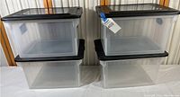 Four clear plastic Sterilite file boxes stacked in two columns with black lids.