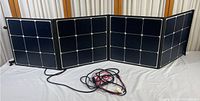 Extended view of four connected panel sections laid flat, showing black solar cells in grid formation and attached cords.