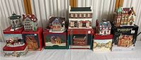 Wide shot of all cottage collectibles displayed on their boxes, showing multiple buildings with painted details and a boxed Victorian Village Christmas set.