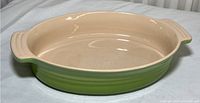 Full view of the oval green and cream stoneware casserole bowl showing round edges and the interior condition.