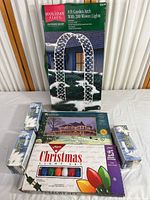 Photo showing all items in the lot including the Holiday Place 8 ft Garden Arch box, three boxes of StarLight outdoor white lights, and one boxed set of Holiday Living colored Christmas lights.