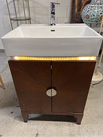 Front view of the freestanding wood vanity with white ceramic sink and chrome faucet. Shows design of vanity doors and lighting under sink.