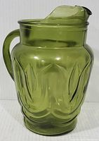 Green glass pitcher with tulip design shown facing front with ice lip visible on the top and a handle on the side.