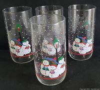 Front view of four clear glasses with colorful snowman winter scenes and lamp posts surrounded by white dots for snow.