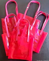Set of ten bright hot pink vinyl tote bags laid together with handles visible, showing shiny, smooth surface and flat bases.