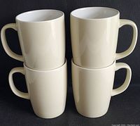 Four stacked two-tone cream tall coffee mugs, showing size and uniformity.