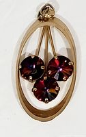 Front view of 1960's oval pendant with three round Aurora Borealis rhinestones visible, gold-tone frame and pronged stone settings.