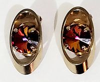 Close-up front view of both oval aurora borealis clip on earrings showing the colorful crystal centers in gold-tone metal frames.