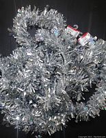 Two silver tinsel Christmas garlands coiled, showing shiny metallic and holographic strands.