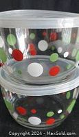 Stacked view of two round glass storage containers featuring Christmas-themed red, green, and white polka dots and translucent plastic lids.
