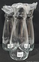 Three clear glass carafes with plastic-wrapped lids, showing manufacturer tags and labels on the base.