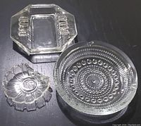 Three vintage glass ashtrays including one round with dot pattern, one rectangular and one leaf-shaped, all clear glass.