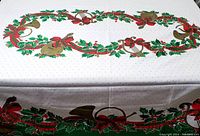 Full view of vintage Christmas tablecloth laid out showing central design with holly garland, red bows, and gold French horns on white fabric with dotted pattern.