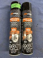 Photo of two black Emzone G4 Brake & Parts Cleaner aerosol cans with orange and white labeling, marked as 'The Big Can', showing product weight and hazard warnings.