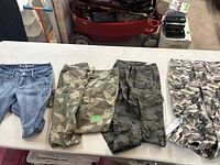 Four pairs of girls pants displayed on a table, three camouflage and one denim.