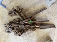 Top view of 4 metal tiedown binders with attached chains and hooks showing rust and wear.