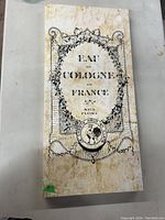 Photo of a rectangular wall hanging artwork featuring 'Eau de Cologne de France' text with floral and emblem decoration in a distressed style.