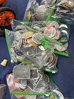 Photo showing multiple ziplock bags filled with assorted pins and buttons, along with several rectangular metal belt buckle-like items on a blue cloth background.