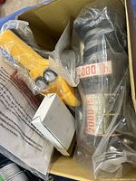 Close-up of electric winch components inside box including motor, cable spool and yellow remote control wrapped in plastic.