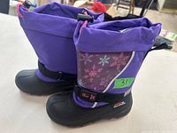 Side view of the pair of purple girls winter boots showing snowflake design and drawstring top