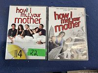 Photo of two DVD sets on blue surface: How I Met Your Mother Complete Season 4 and Season 2 cases, showing front cover art and labels.